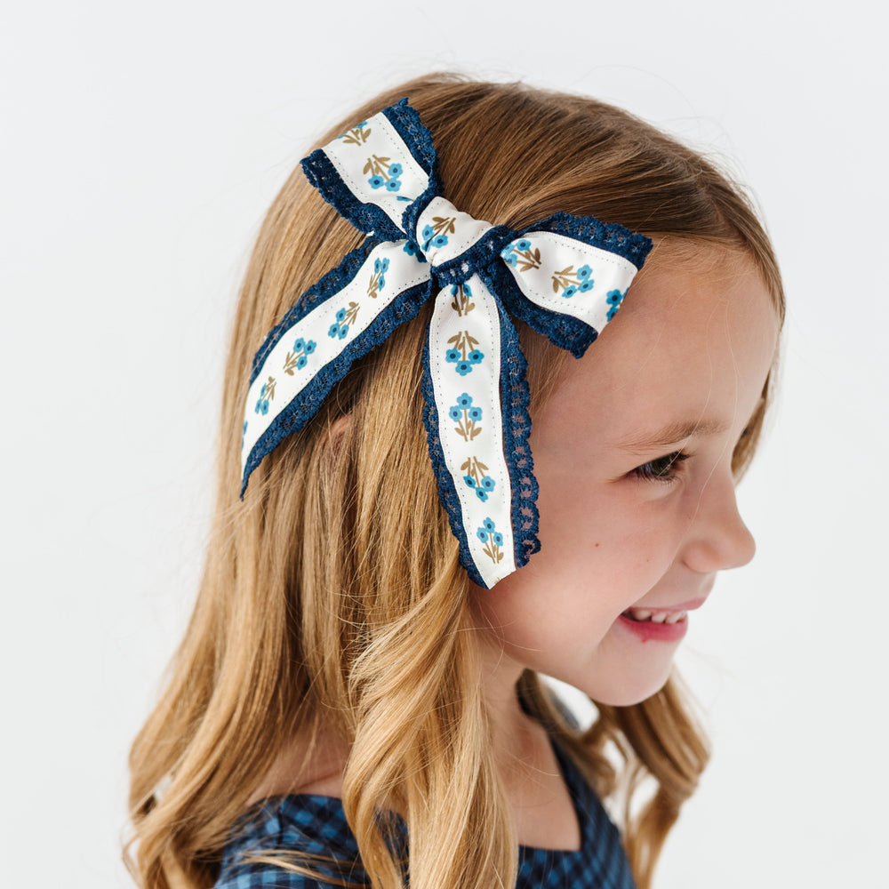 little girl with blue floral hair bow with navy trim paired with matching blue gingham fall twirl dress