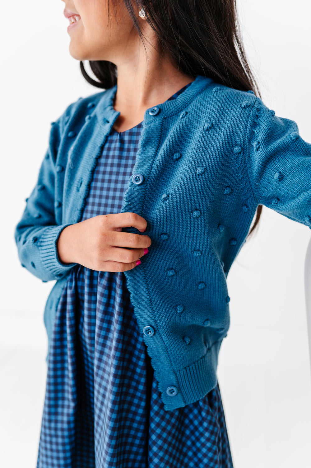 close-up girl wearing blue bubble knit sweater paired with matching blue gingham v-neck twirl dress 