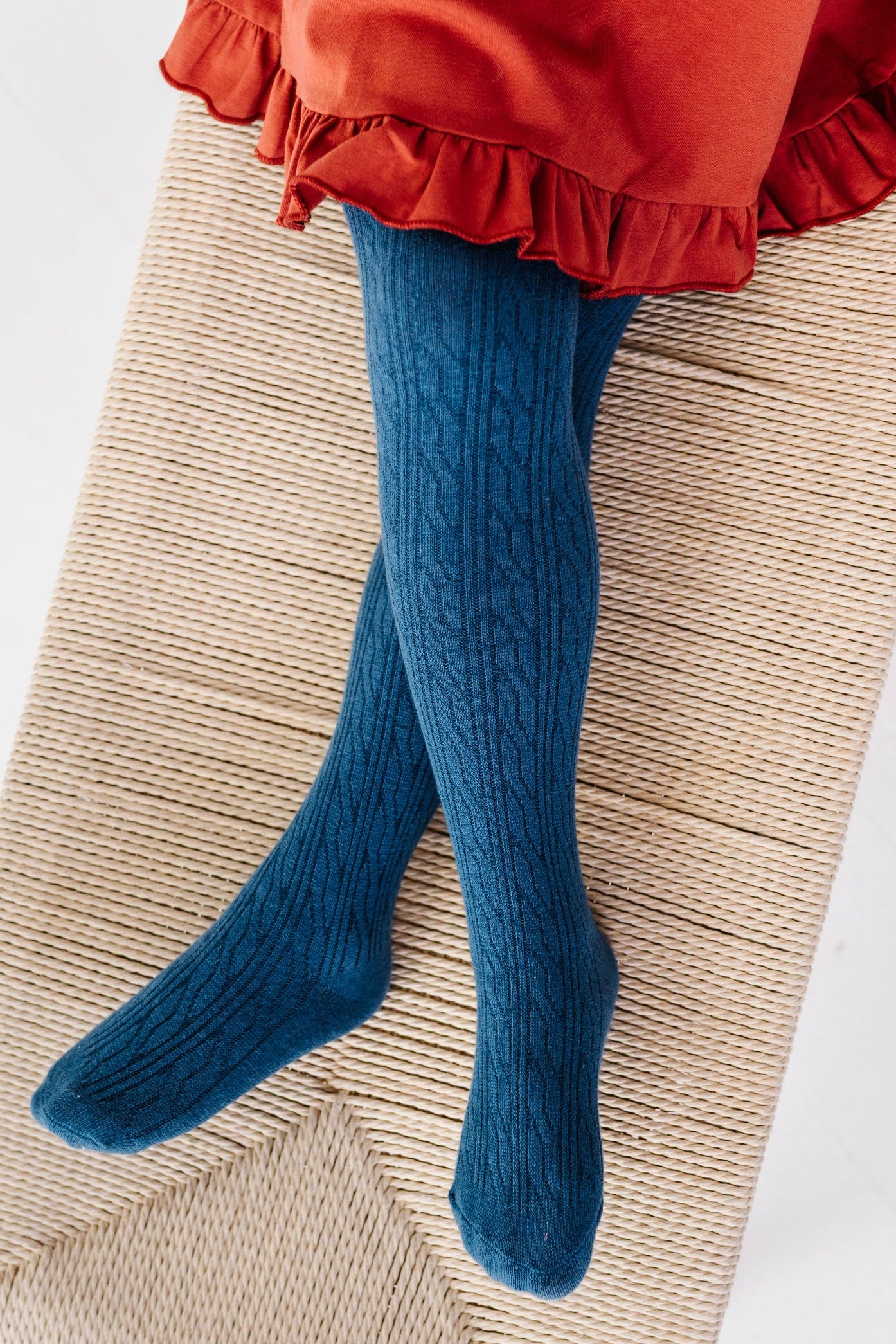 young girl sitting on bench in blue cable knit tights paired with rust ruffle hem twirl dress for fall
