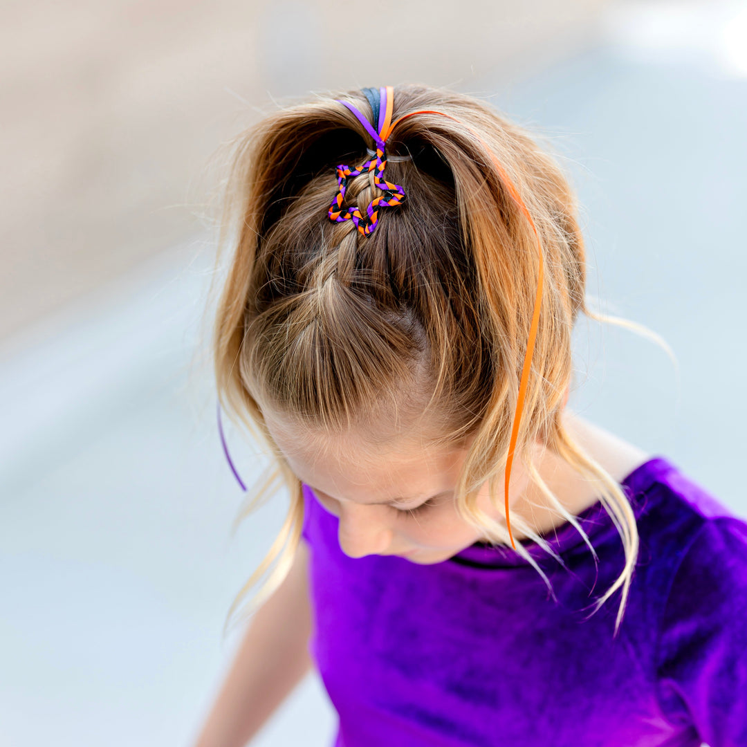 girl with Halloween braided star snap clip on ponytail featuring orange, black and purple ribbon with tail paired with matching purple velvet top