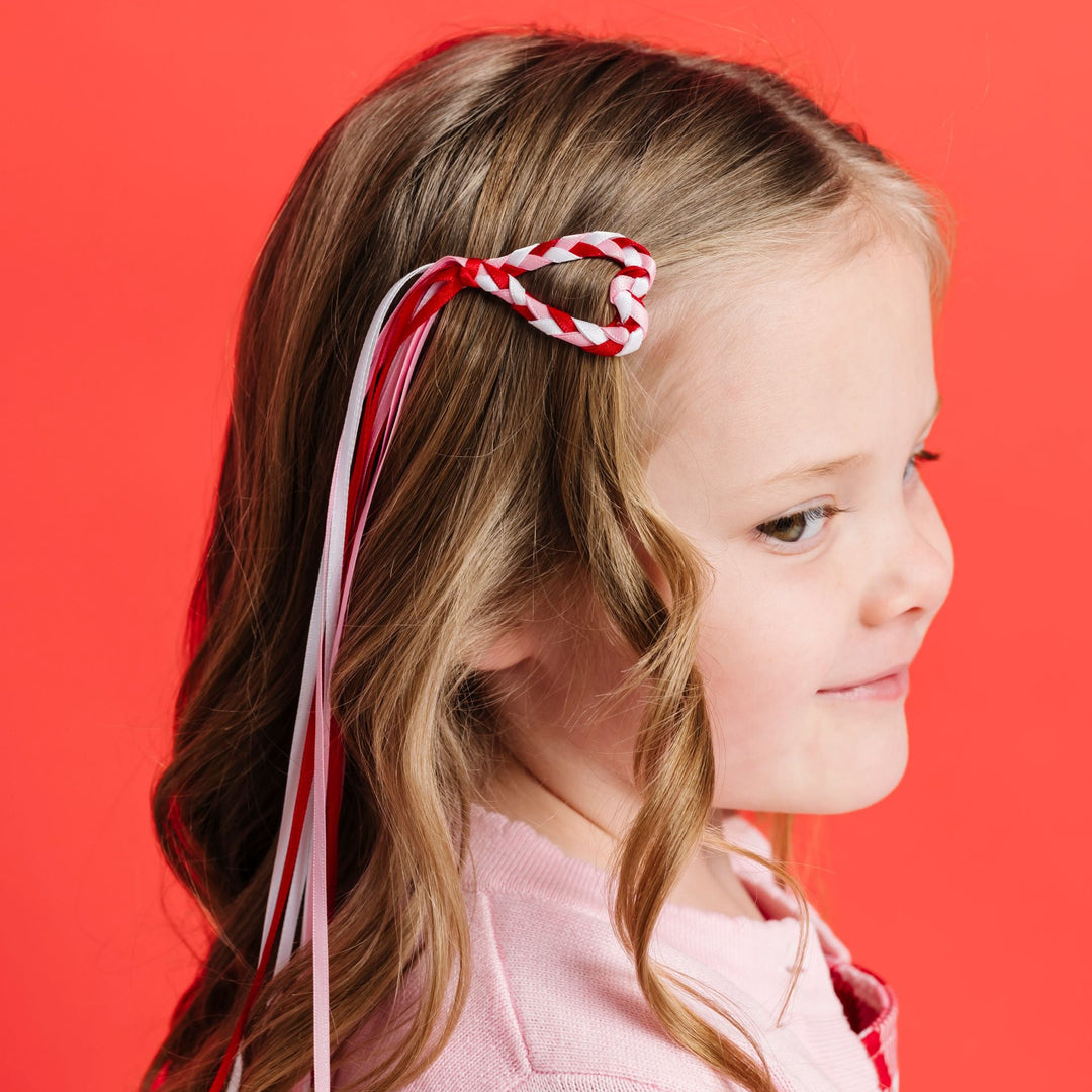 little girl in heart shaped snap clip with braded pink, white and red ribbon with a long streamer tail