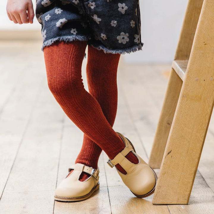 girl standing by ladder in Brick red cable knit tights made by little stocking co