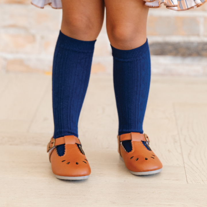 little girl in bright navy cable knit knee highs and brown leather shoes