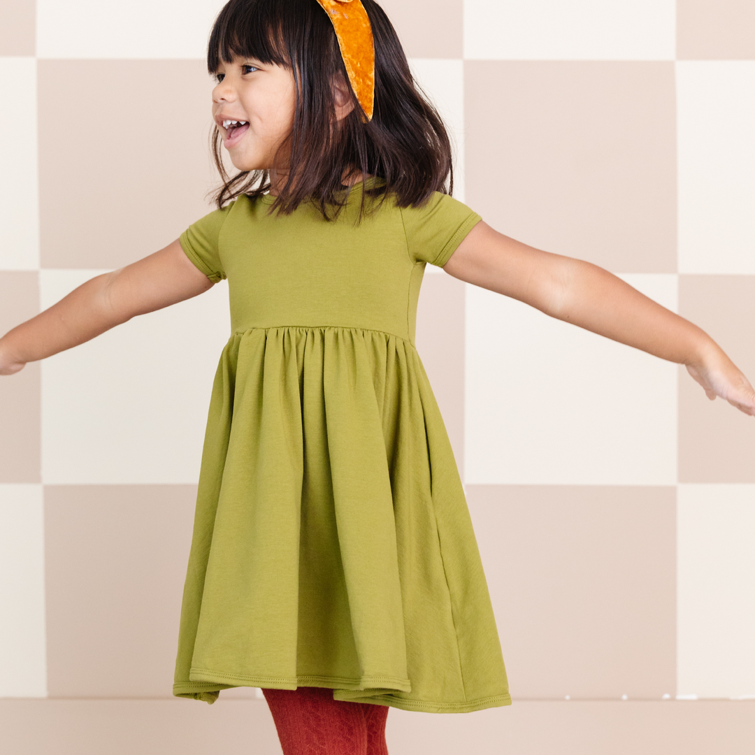 little girl wearing bright olive green cotton pocket dress and yellow velvet headband