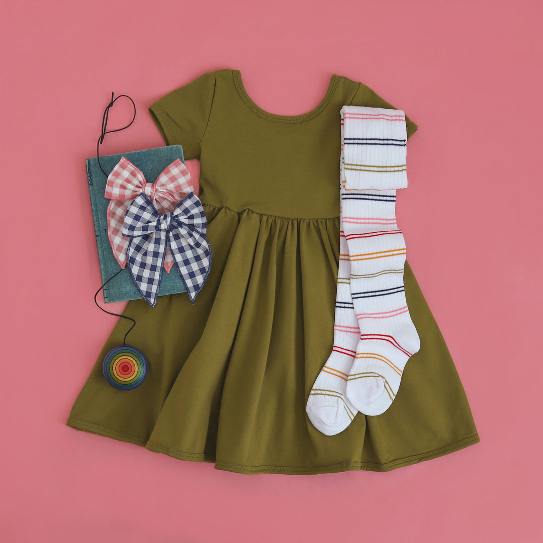 bright olive green girls cotton pocket dress styled with rainbow striped ribbed tights and colorful gingham hair bows