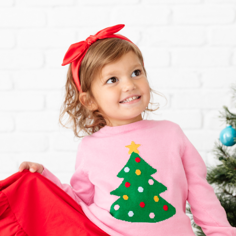 little girl in pink tree sweater with bright red satin headband 