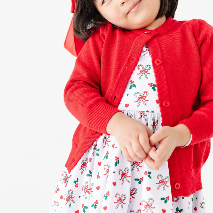 little girl in bright red sparkle knit Christmas cardigan and matching candy cane dress