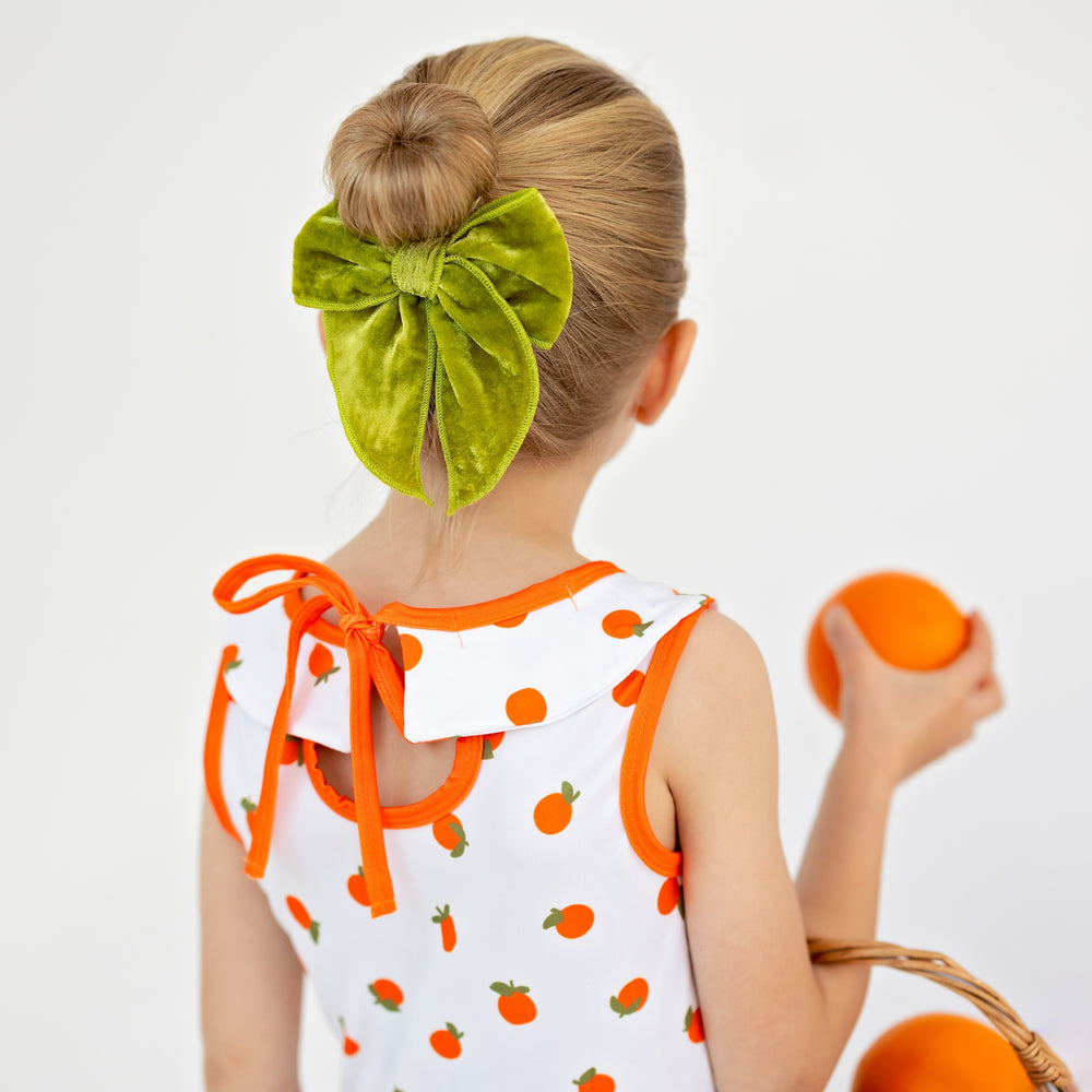 little girl wearing cute oranges dress with bright olive green velvet hair bow in her hair