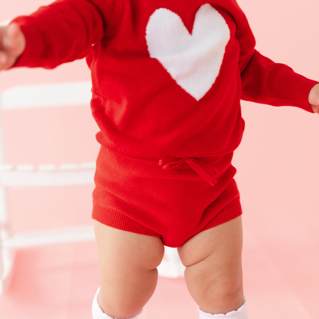 close-up of baby girl in bright red heart sweater and matching red cotton knit sweater bloomers with heart knee highs