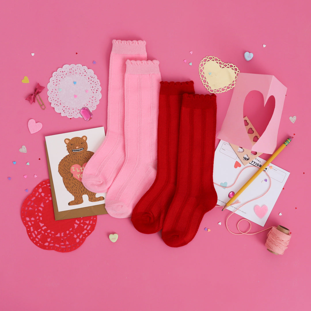 flat lay of two pairs of scallop trimmed knee high socks in pink and red with class Valentine's cards