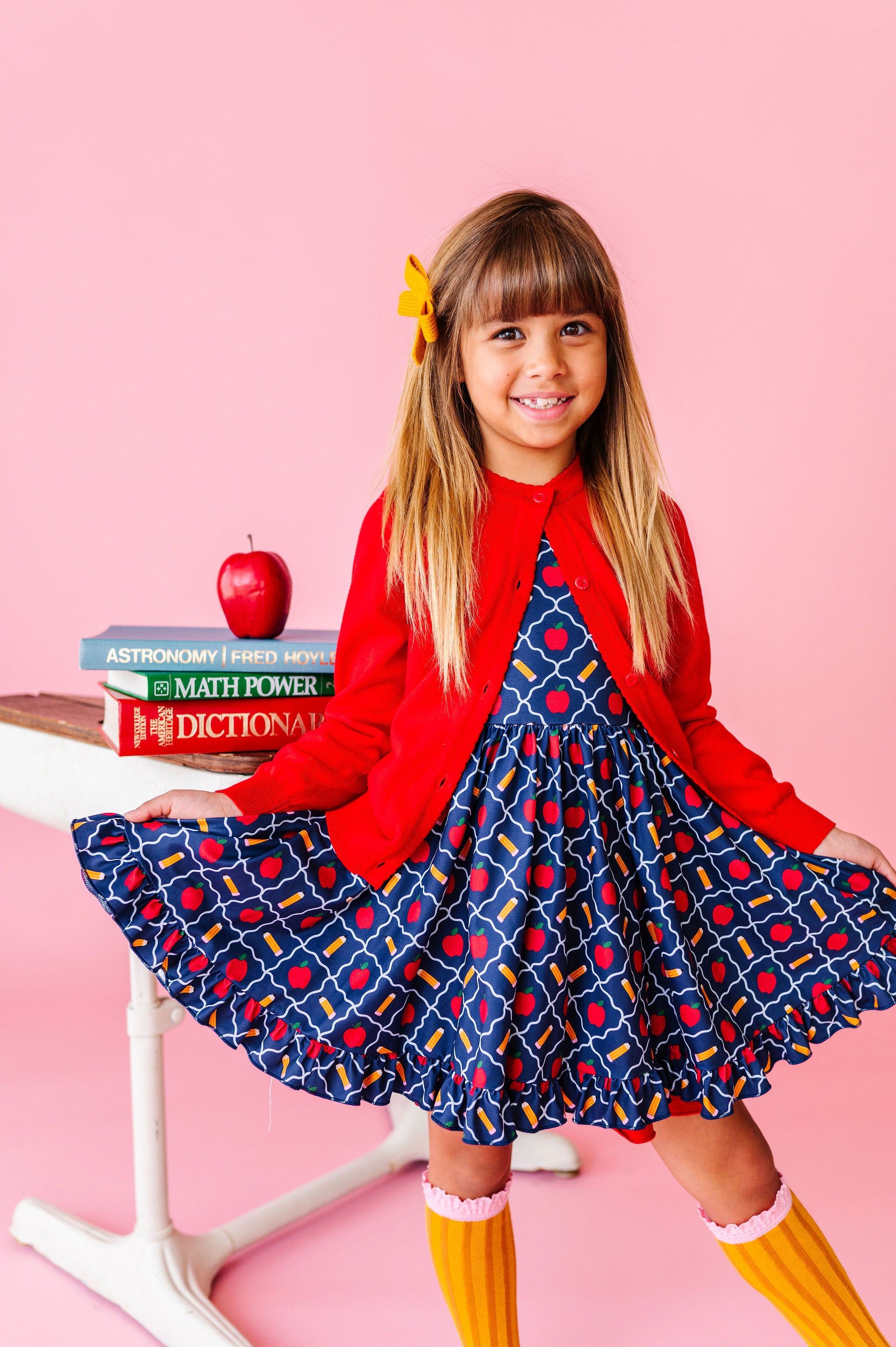 little girl in navy apple and pecile print twirl dress paired with pencil knee socks and bright red cotton knit cardigan for school