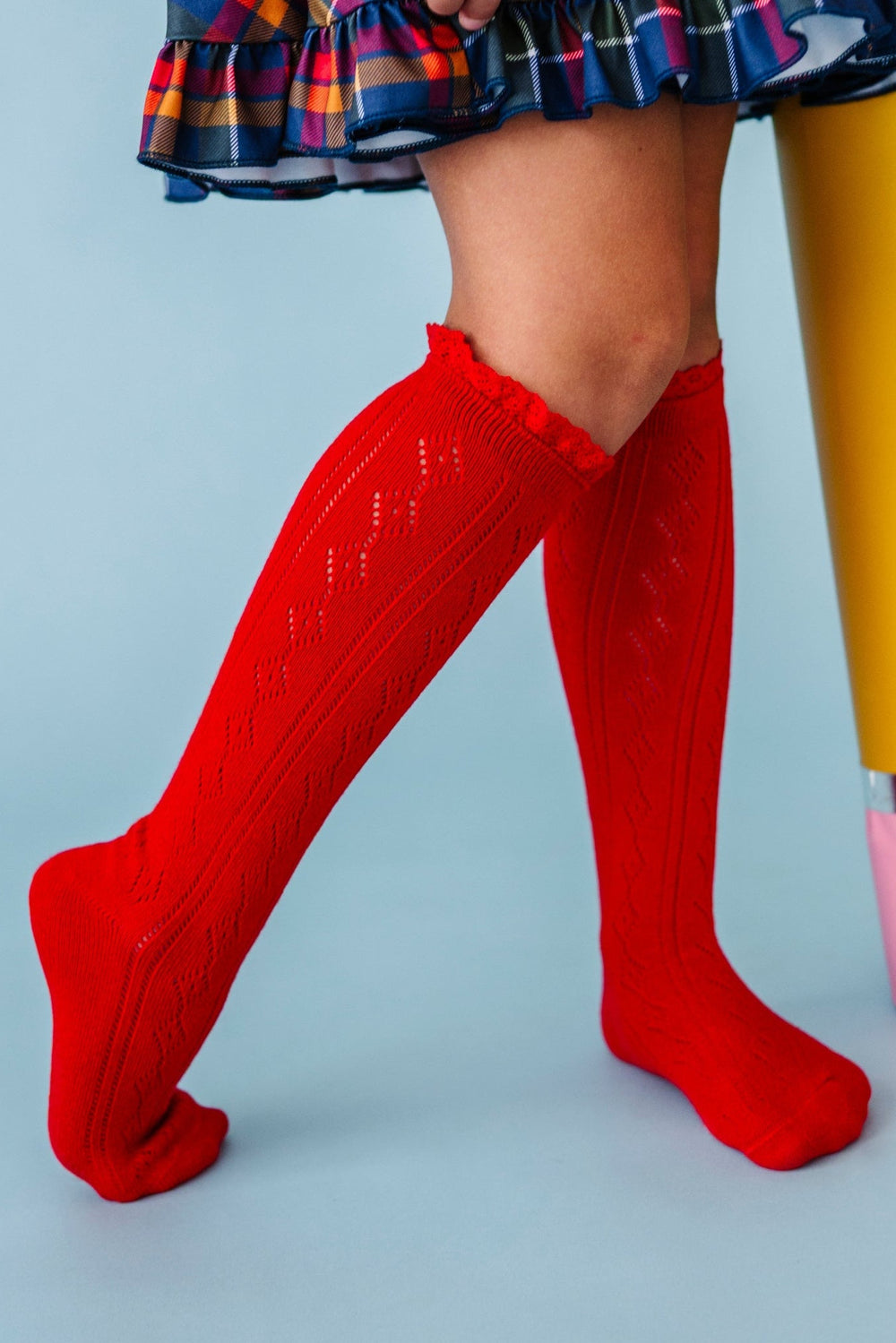 girl holding giant pencil prop in bright red pointelle lace top knee socks and navy plaid school dress