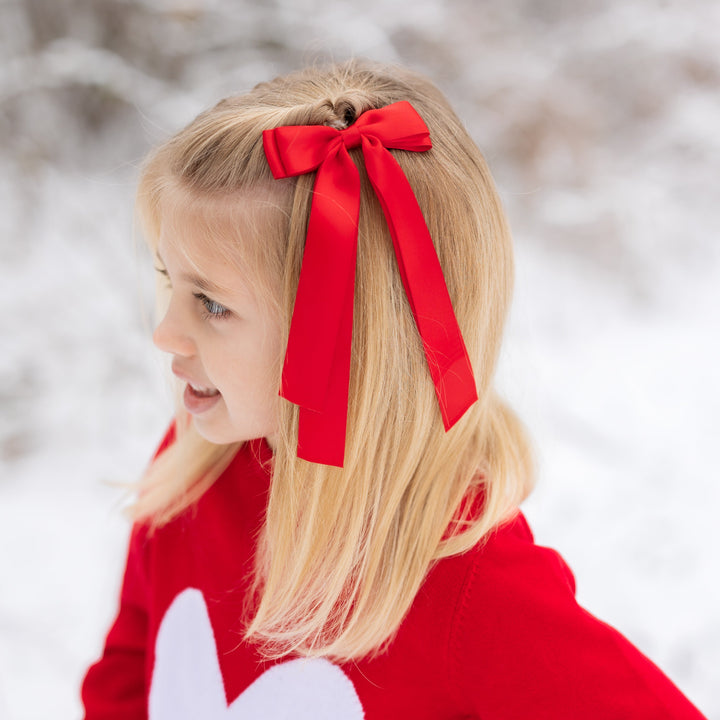 little girl with bright red long tail ribbon bow on clip and matching red Valentine's sweater