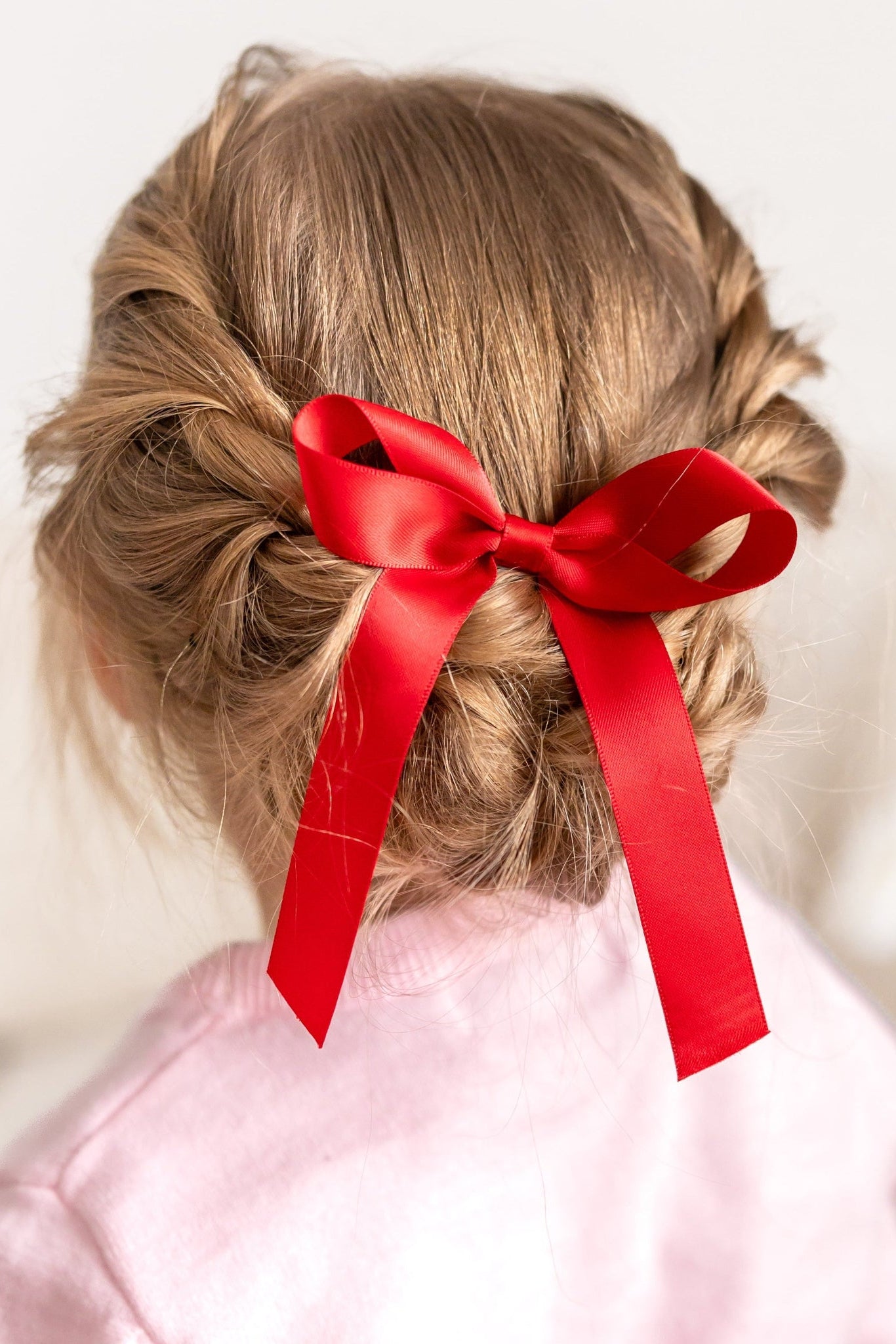 little girl with braided hair wearing bright red satin hair bow on clip 