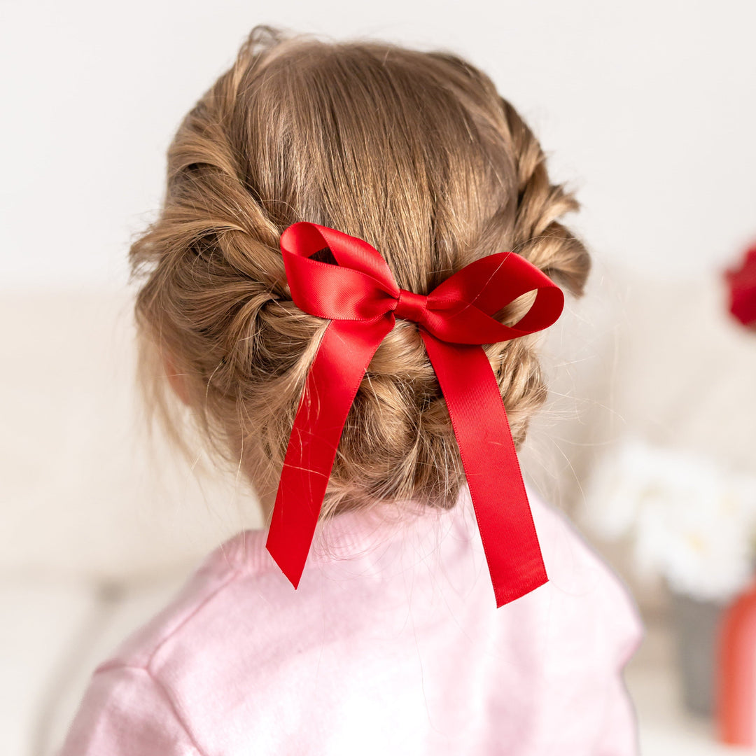 little girl with braided hair wearing bright red satin hair bow on clip 