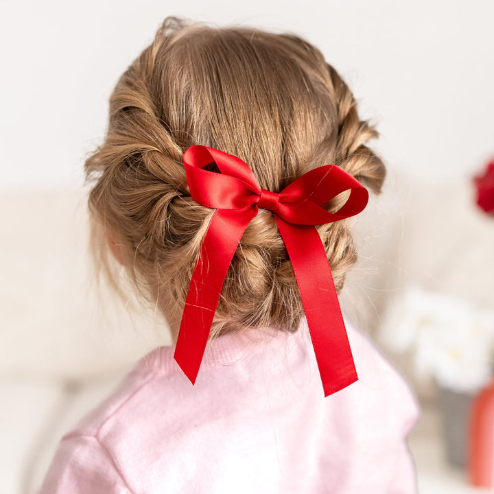 little girl with braided hair wearing bright red satin hair bow on clip 