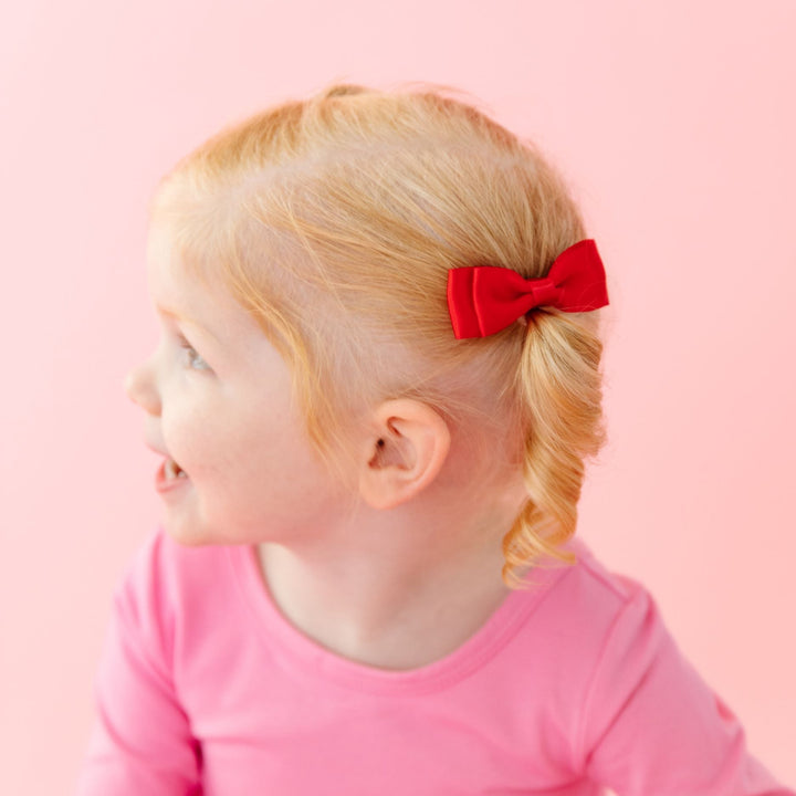 little girl in pink cotton twirl dress and coordinating red satin pigtail bows