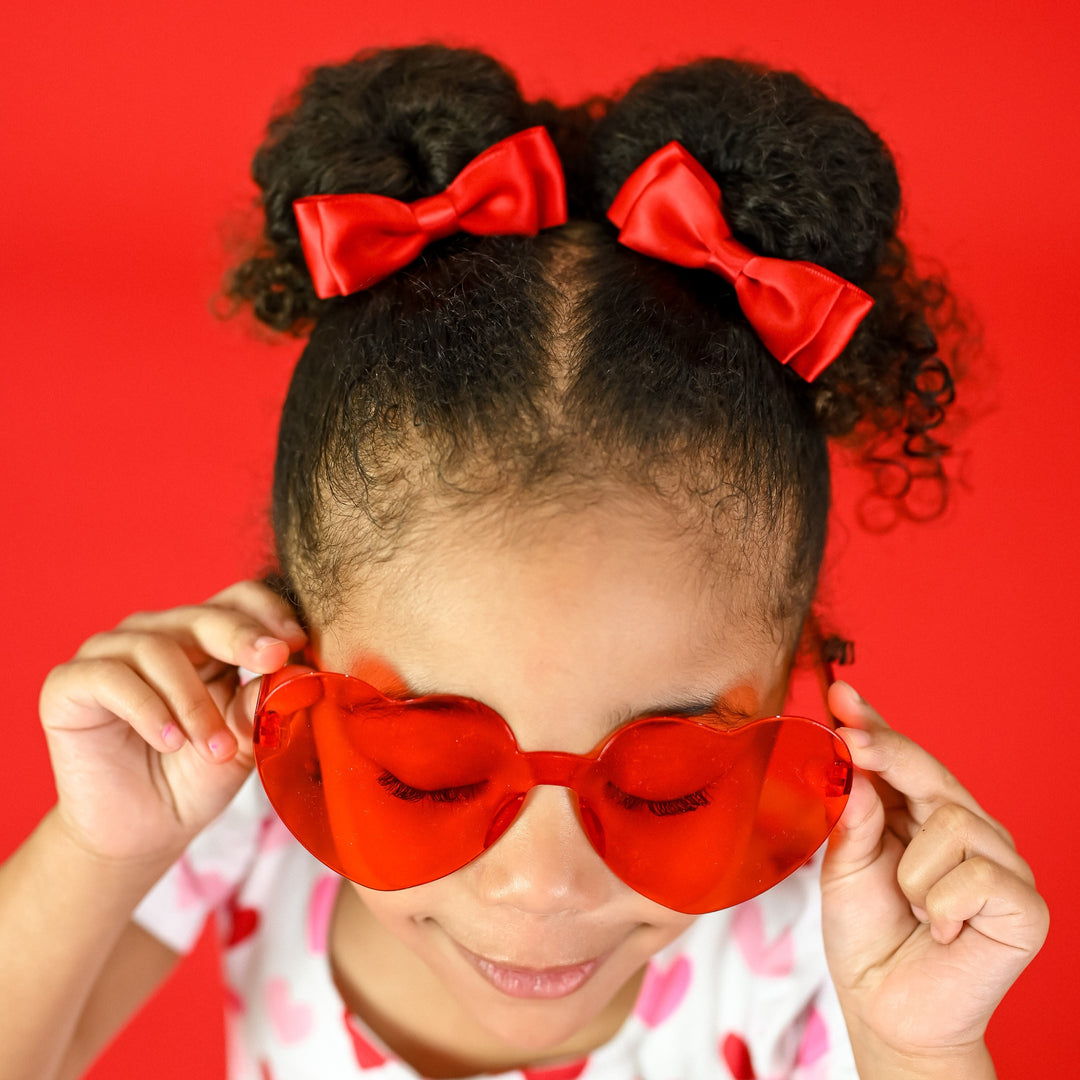 little girl in heart sunnies wearing red and pink heart dress with matching bright red satin pigtail bows on clips