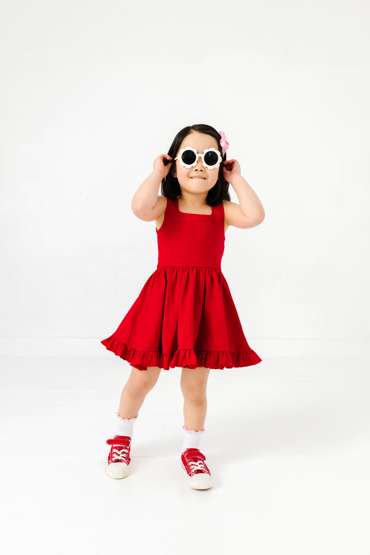 little girl in flower sunglasses wearing bright red summer sleeveless twirl dress with red sneaks, blossom lettuce trimmed midi socks and blossom satin bow
