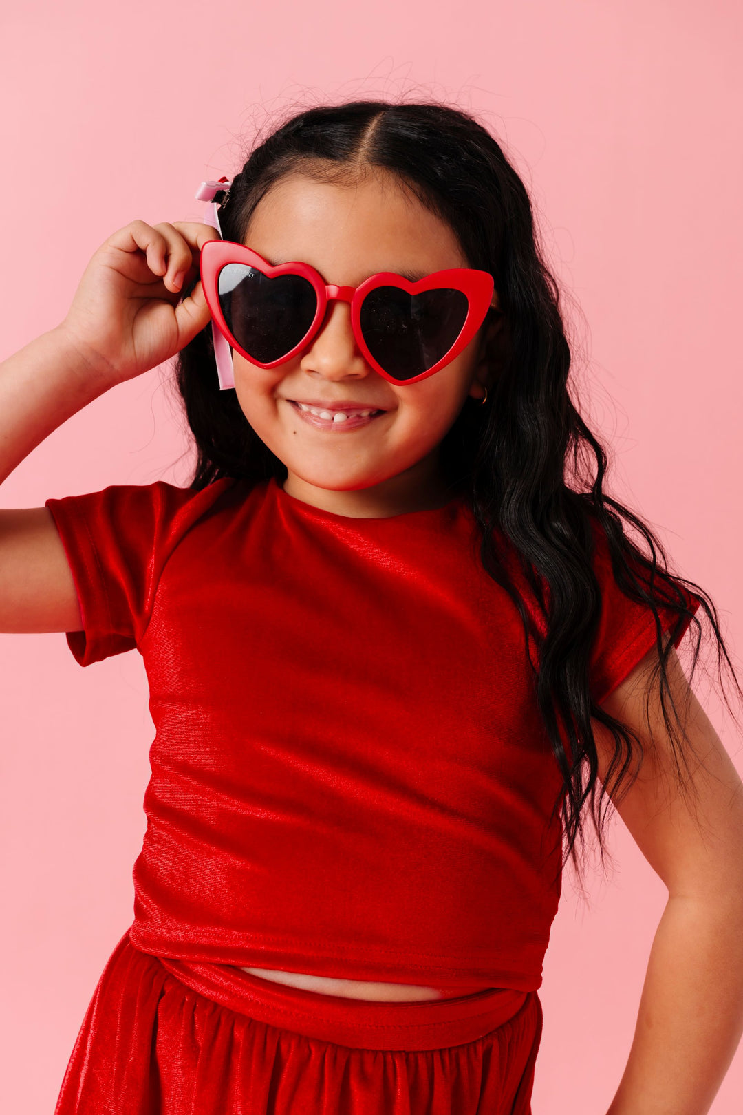 girl in red heart sunglasses and red velvet top with bow tie at the back paired with matching velvet skort