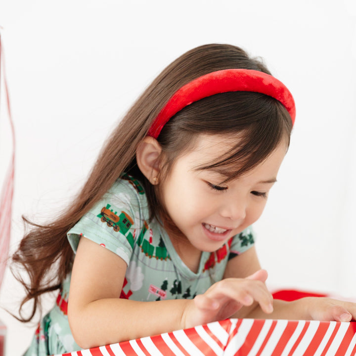 Little girl in bright red plush headband and Christmas train dress