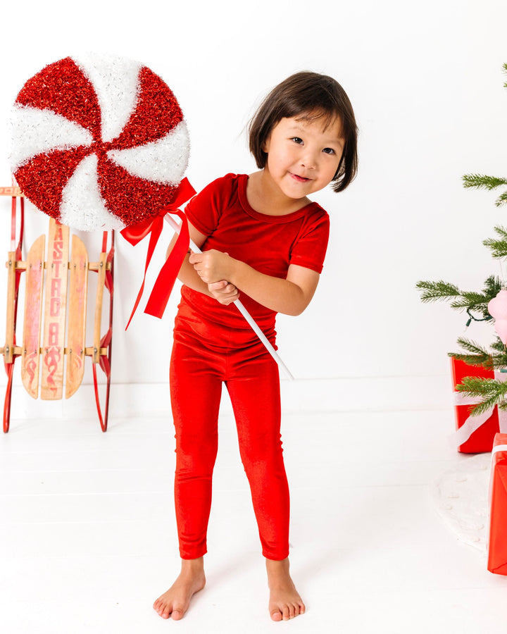 little girl holding giant peppermint in bright red fitted velvet top and legging set for Christmas