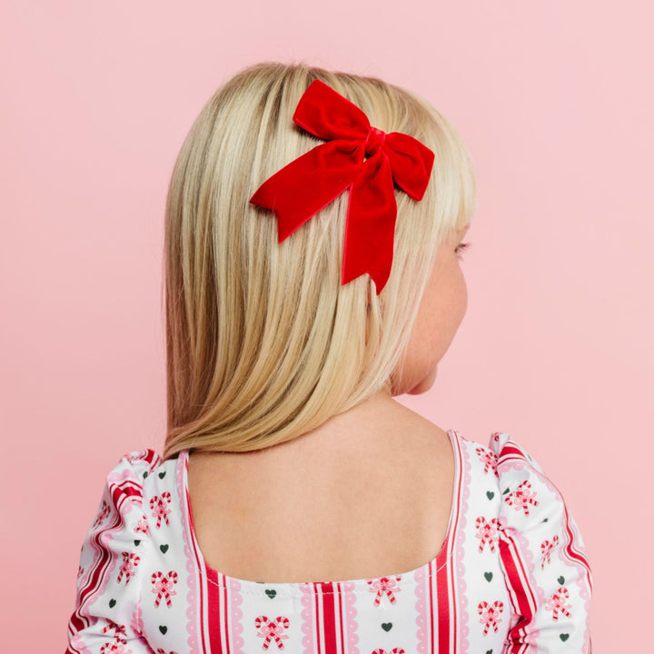 little girl in candy cane print square neck twirl dress with matching bright red velvet ribbon bow on clip