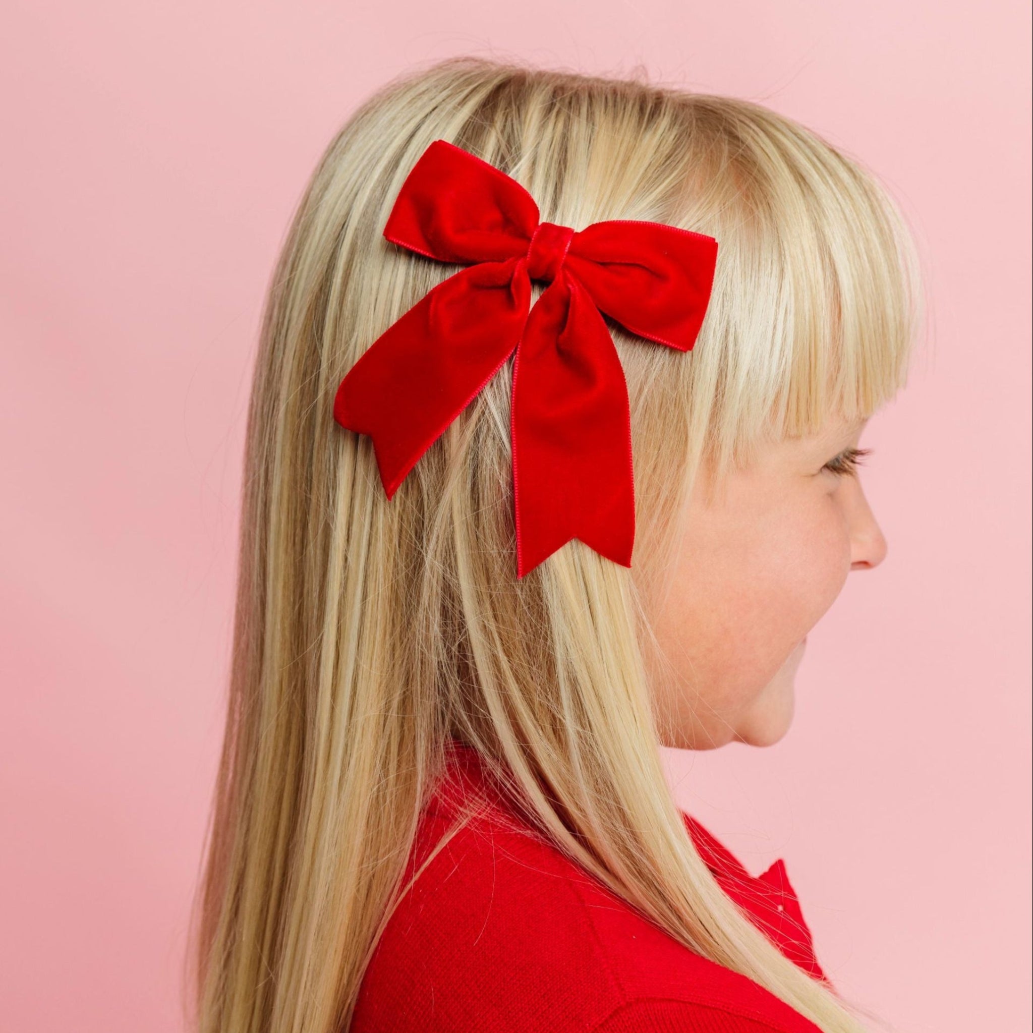 young girl in red Christmas cardigan paired with bright red velvet ribbon bow on clip 