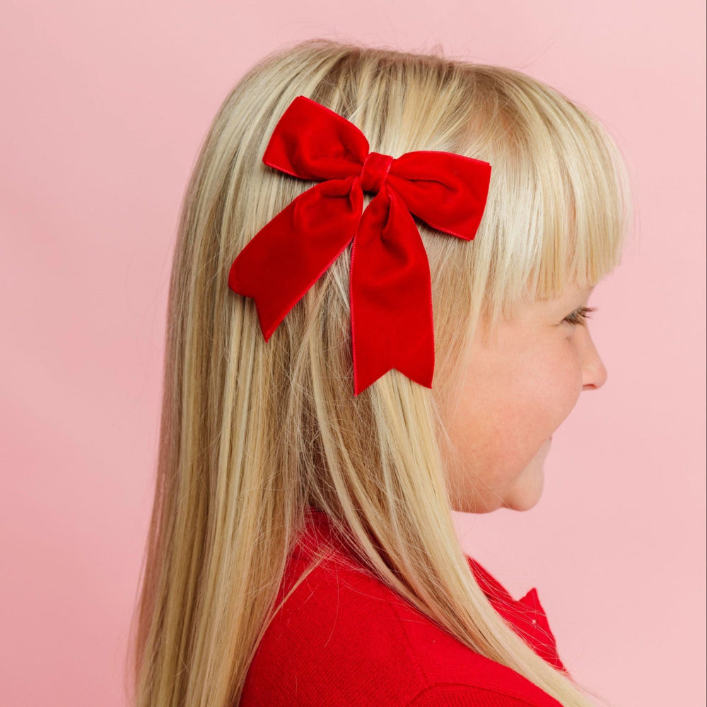 young girl in red Christmas cardigan paired with bright red velvet ribbon bow on clip 