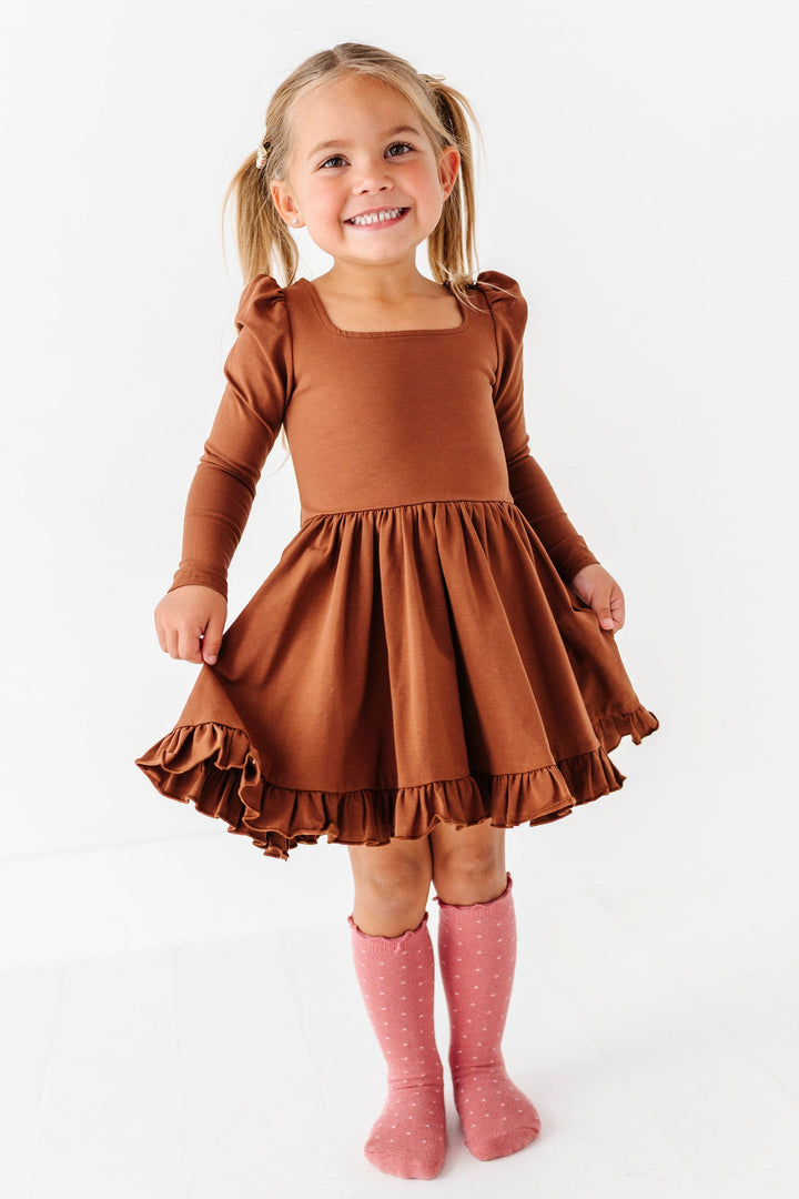 little girl wearing solid brown cotton twirl dress with long sleeves, ruffle trim and square neckline 