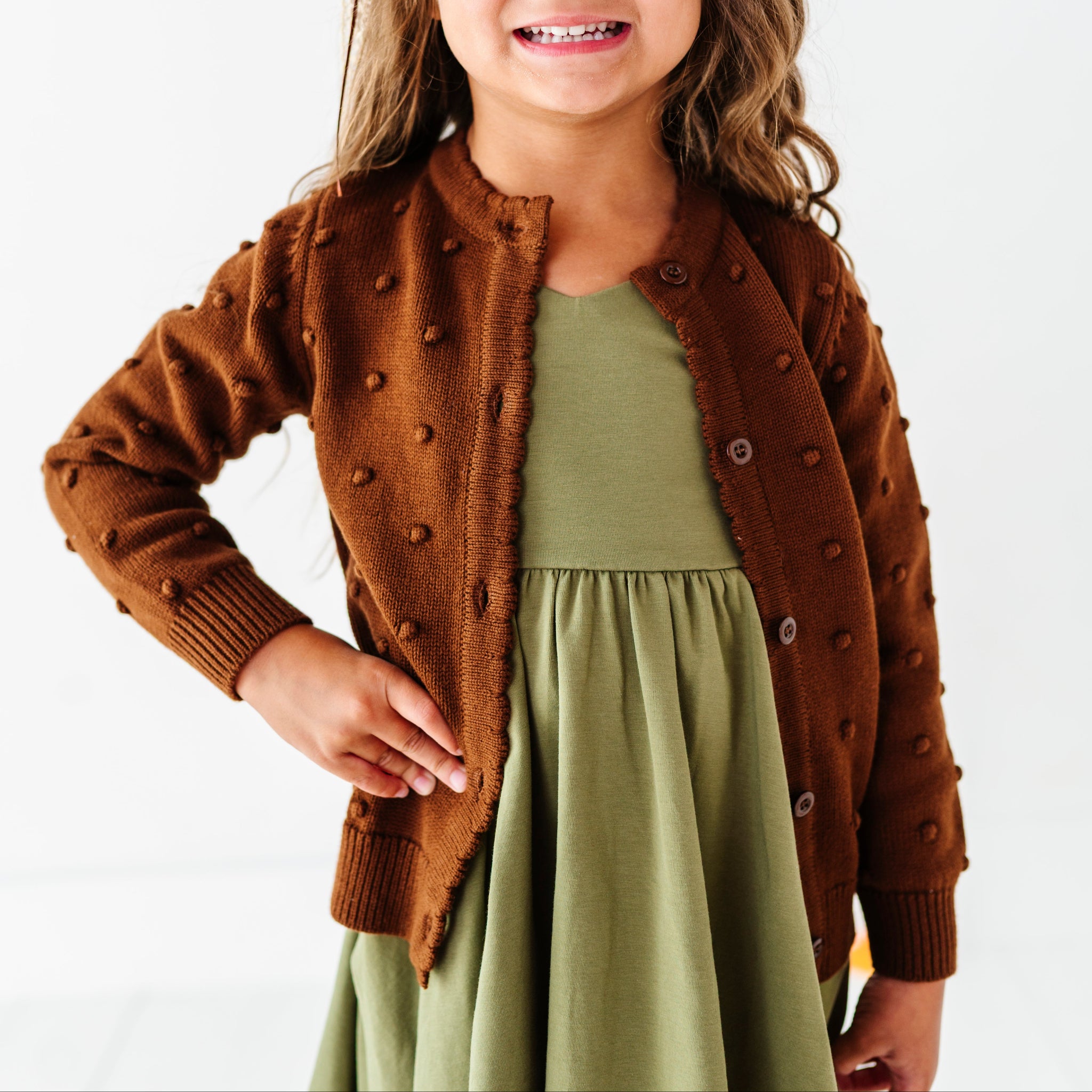 young girl in olive green v-neck twirl dress paired with brown cotton knit cardigan with raised bubble texture