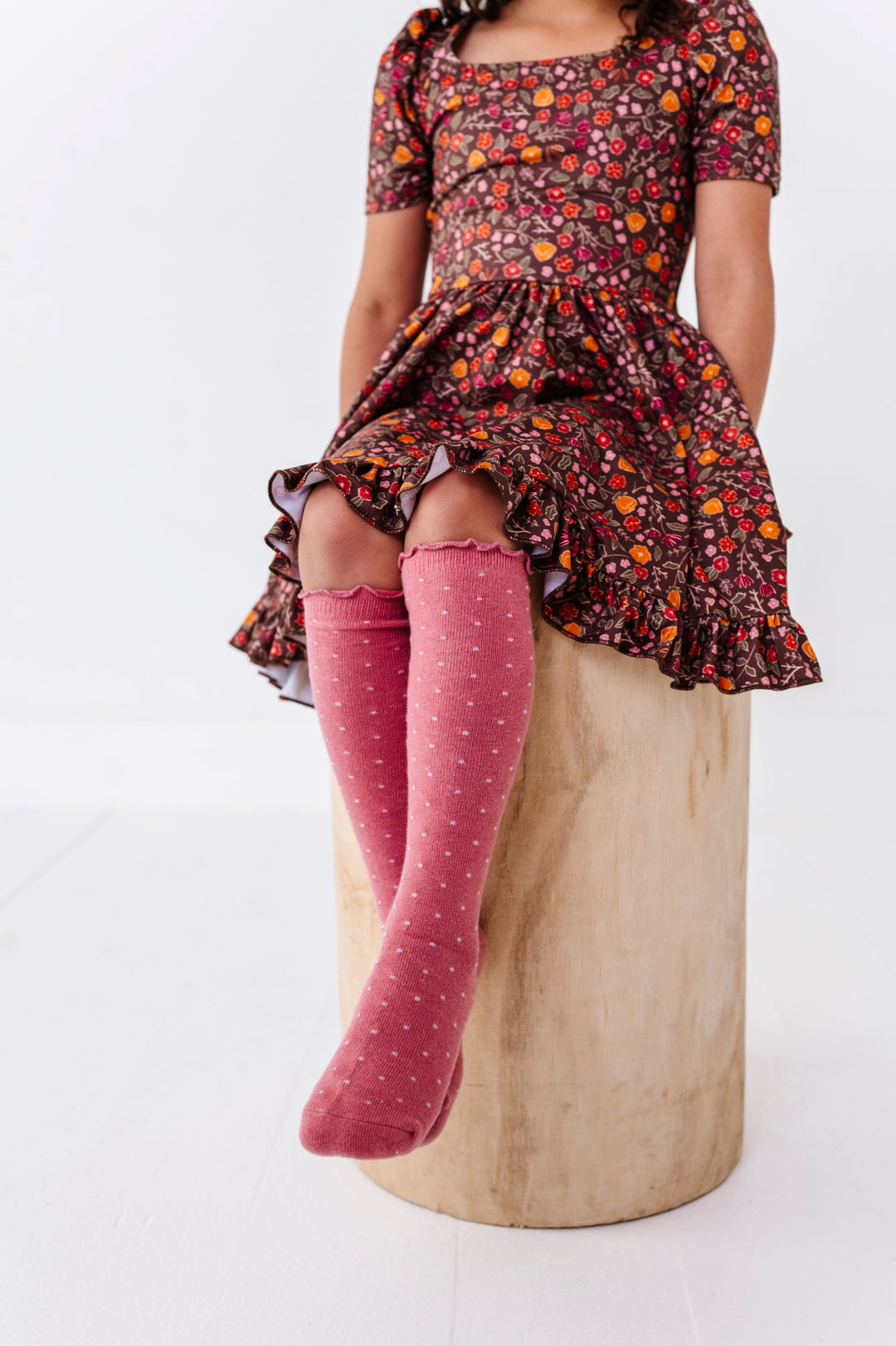 little girl sitting on stool in short sleeve brown floral fall twirl dress paired with matching pink knee socks with lettuce trim and cream dots