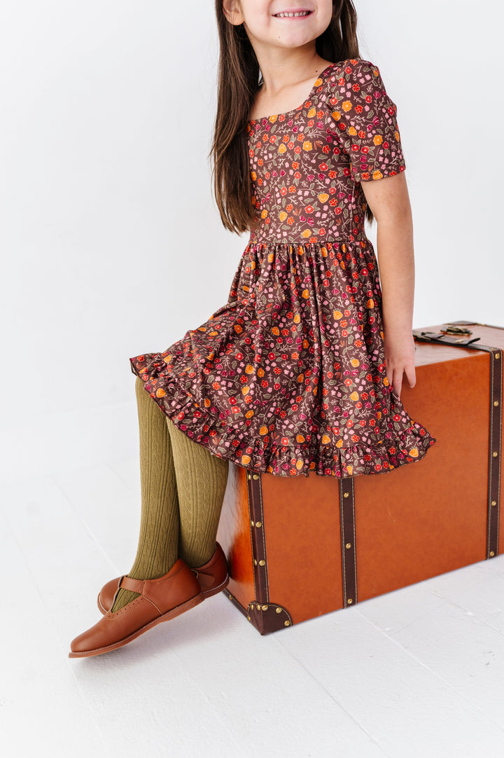 young girl sitting on vintage suitcase in brown floral dress paired with coordinating olive cable knit knee socks