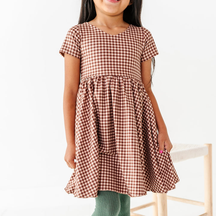 young girl in two-tone v-neck twirl dress in brown gingham with sage green tights
