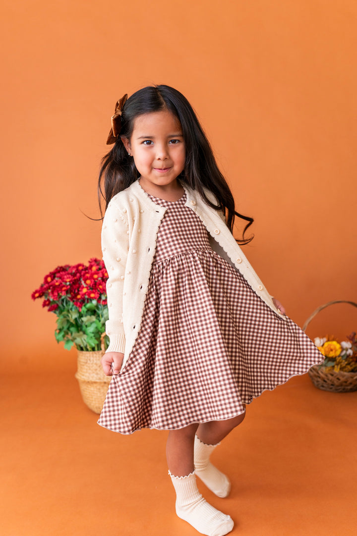 little girl twirling in brown gingham twirl dress and cream sweater and midi socks