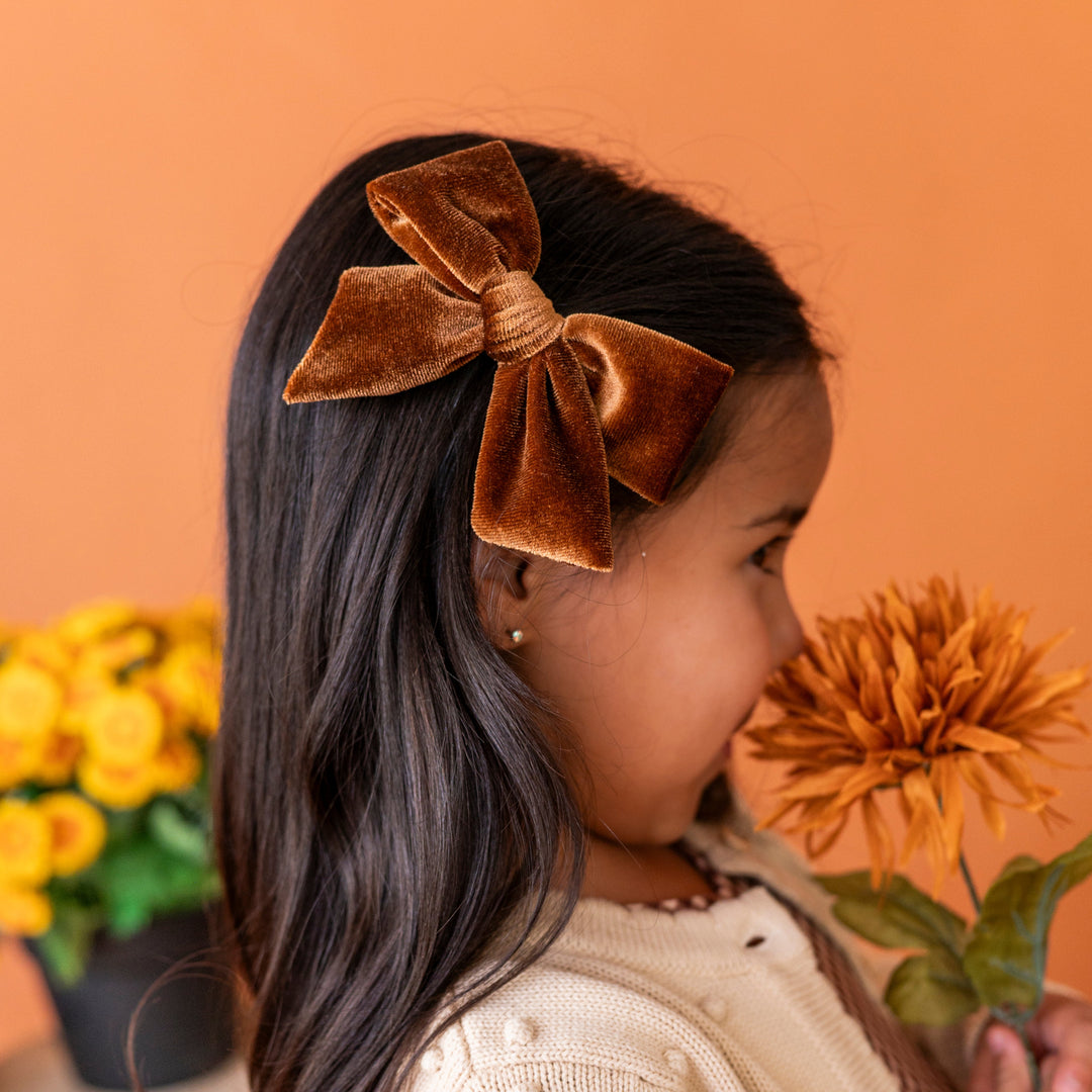 little girl with fall flower wearing golden brown velvet bow on alligator clip and cream cardigan