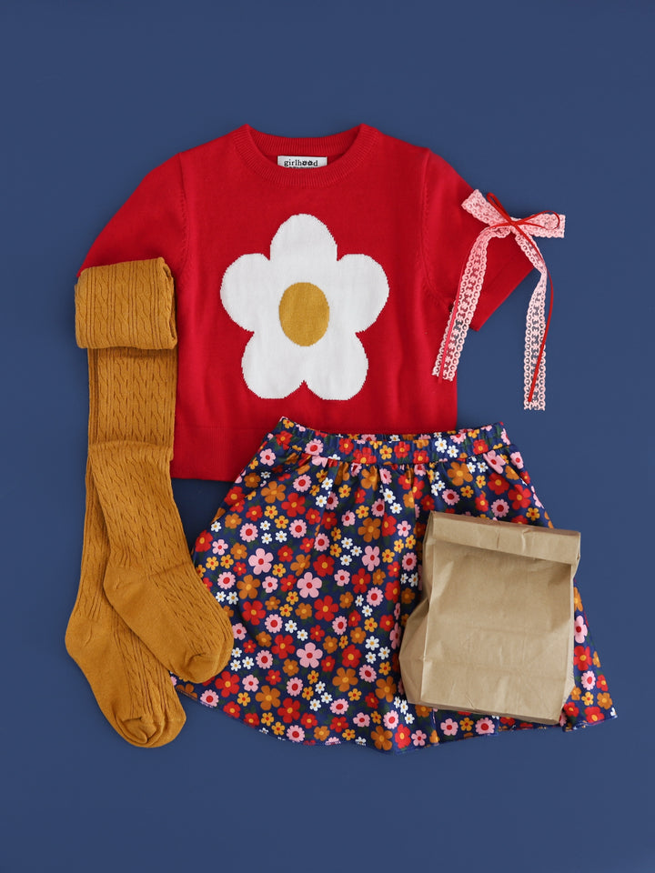 flatlay of girls back to school outfit with red short sleeve sweater with white flower, matching floral skort, mustard cable knit tights and lace and ribbon pink and red bow
