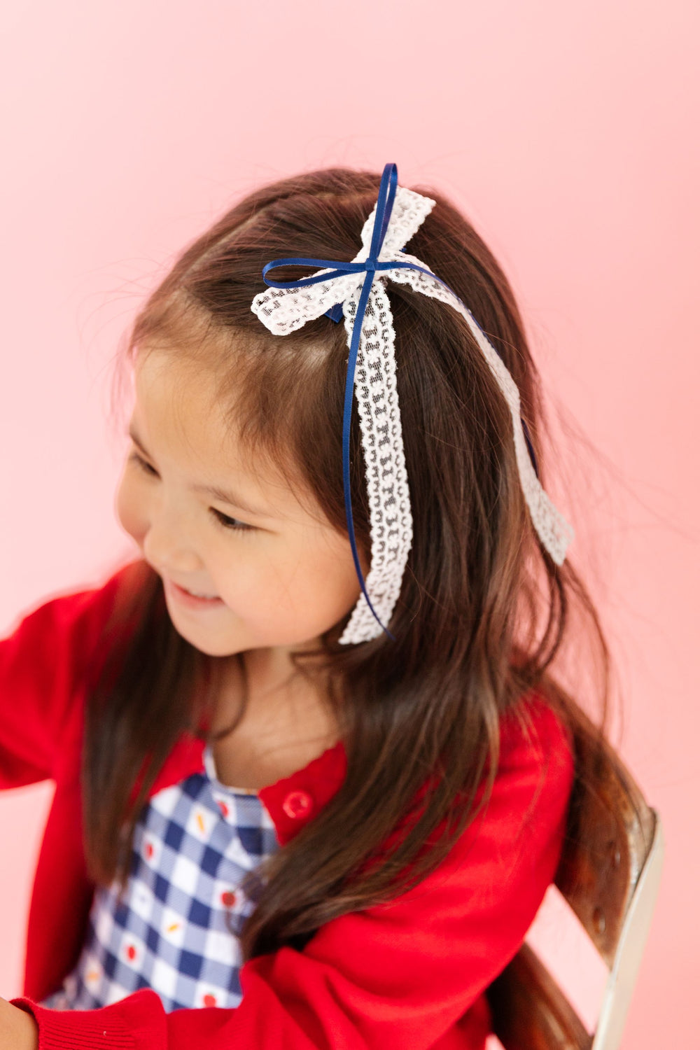 little girl in white lace long tail bow with navy ribbon overlay paired with gingham back to school dress and red cardigan