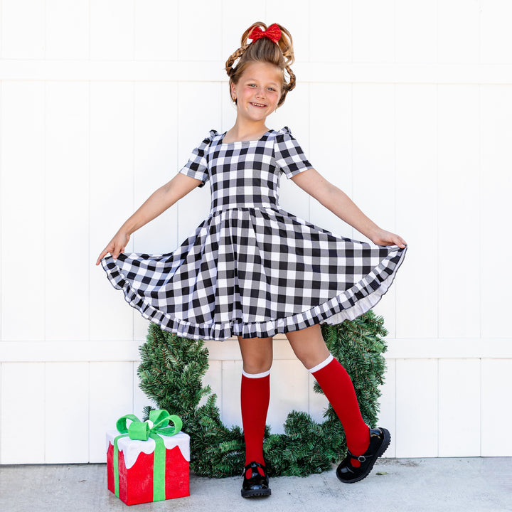 little girl in black and white buffalo plaid twirl dress, sparkly red bow and red with white trim Santa inspired knee high socks for Christmas