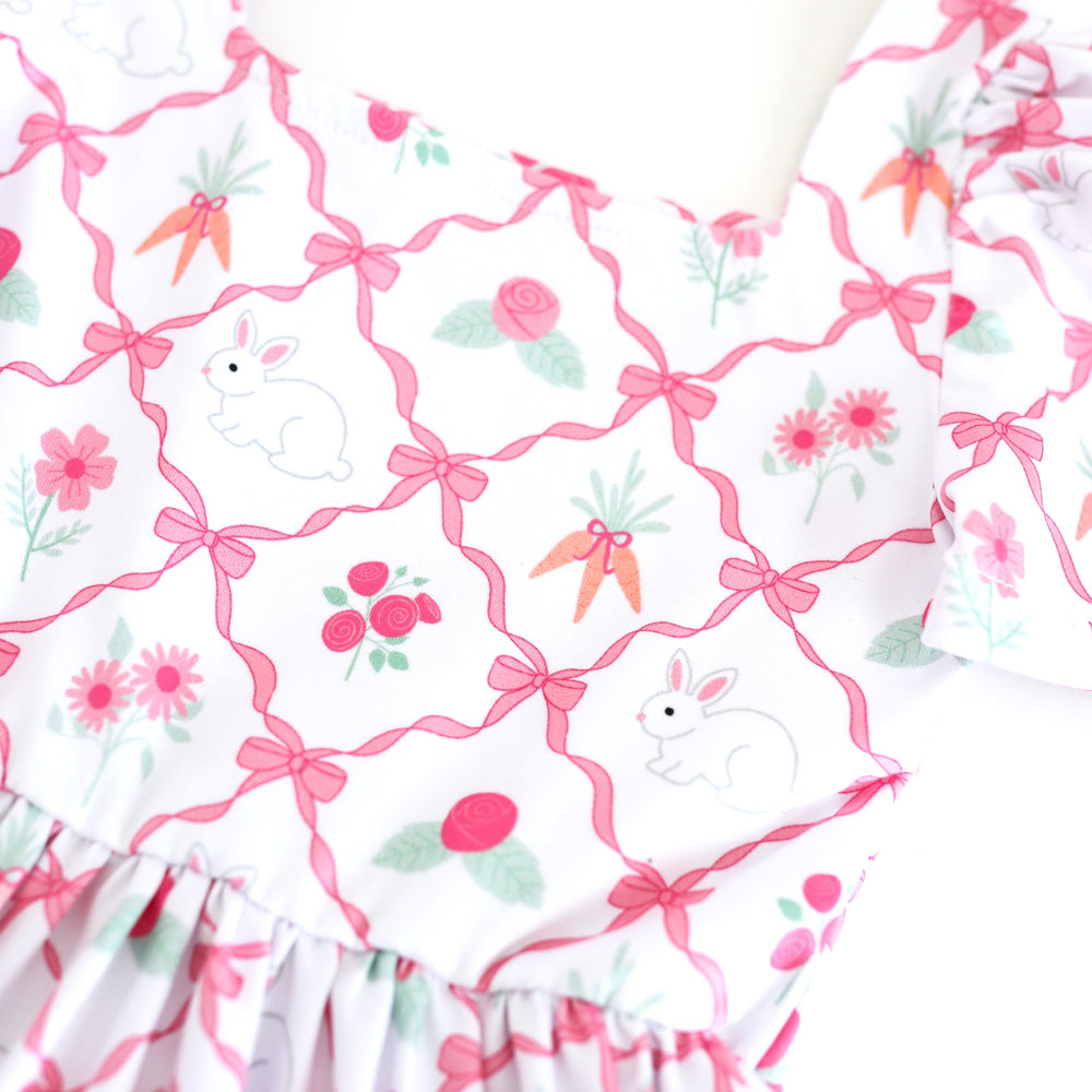 closeup of pink ribbon print with bunnies, pink spring flowers and carrots on white base for Easter