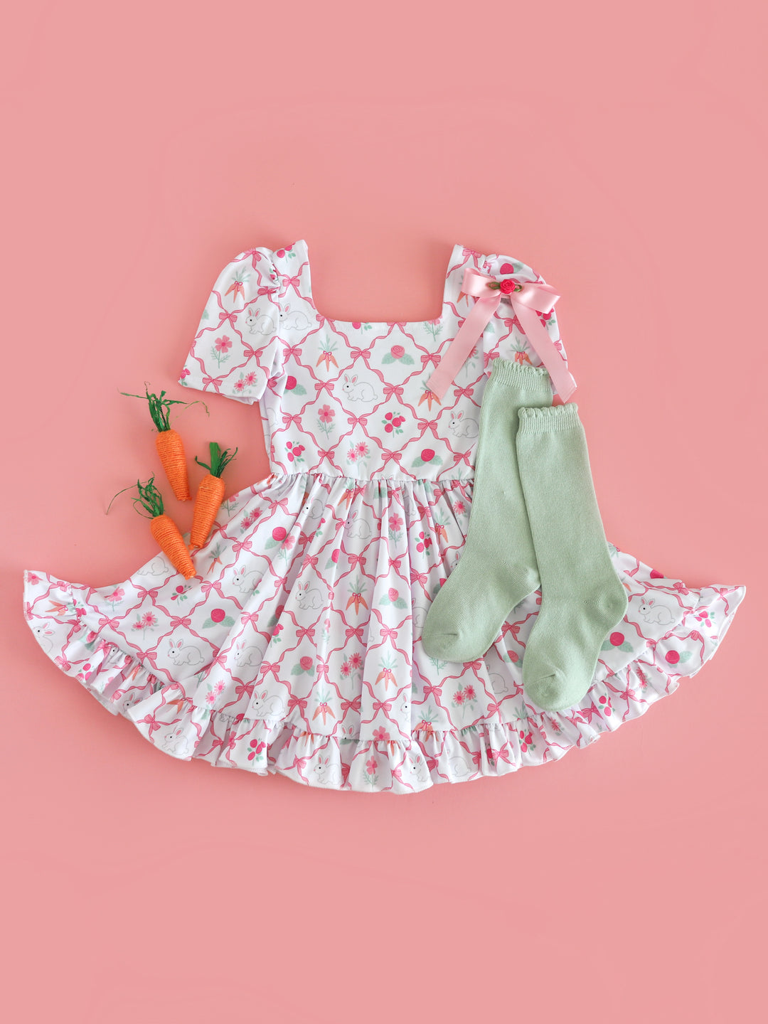 flat lay of girls' white easter dress with pink ribbon pattern, bunnies, flowers and carrots for Easter styled with matching satin rosette bow and mint scalloped knee socks