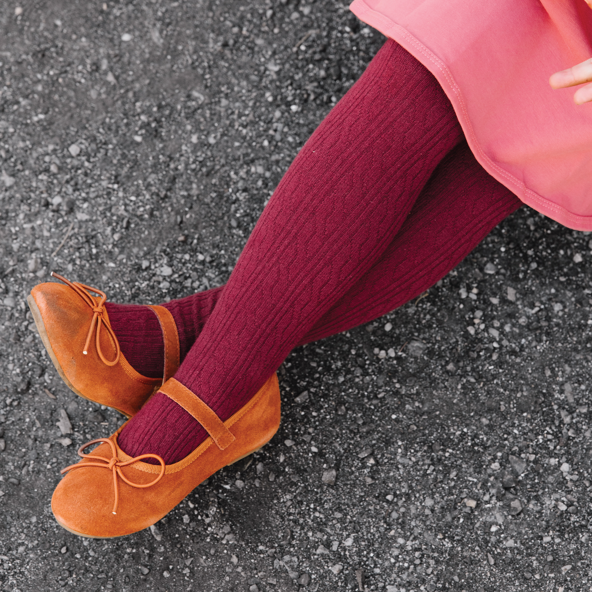 little girl sitting wearing burgundy cable knit tights and pink dress and brown suede shoes