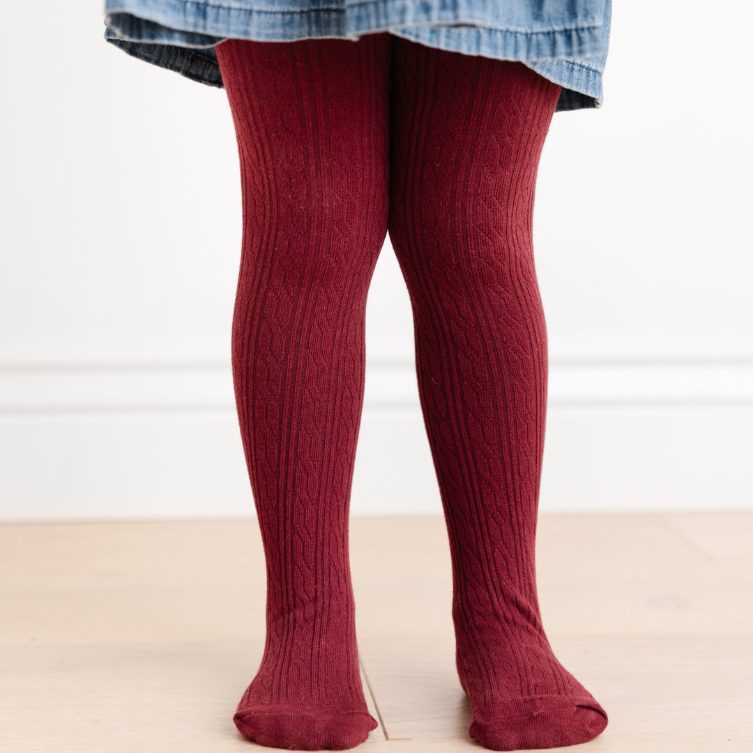 little girl standing wearing burgundy cable knit tights