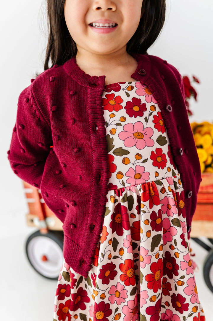 little girl wearing twirl dress with fall flowers paired with coordinating burgundy bubble knit cardigan