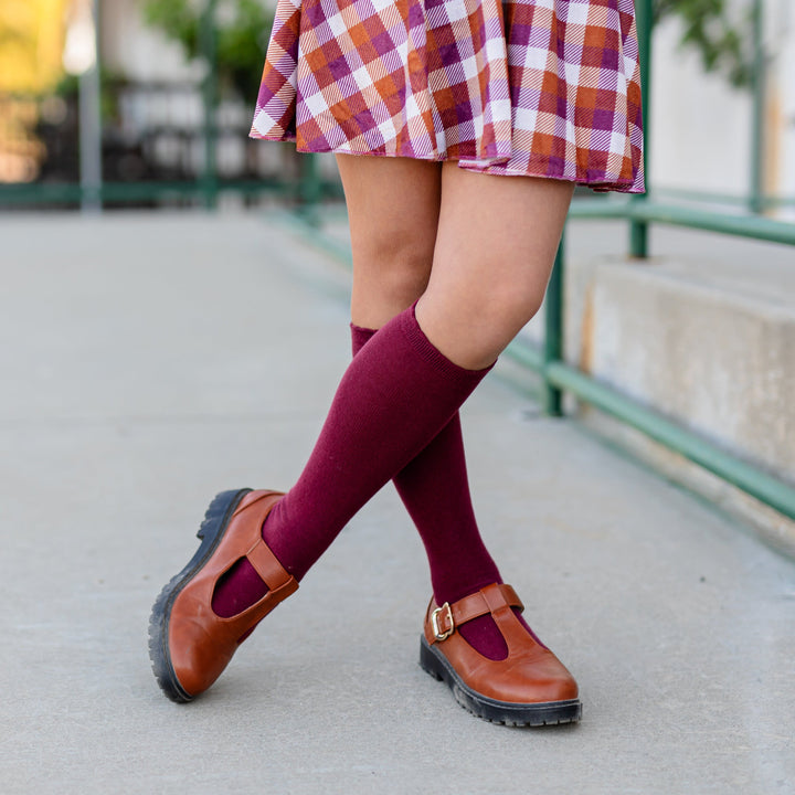 little girl in burgundy knee highs socks with scalloped trim paired with brown mary janes and velvet fall plaid skort  