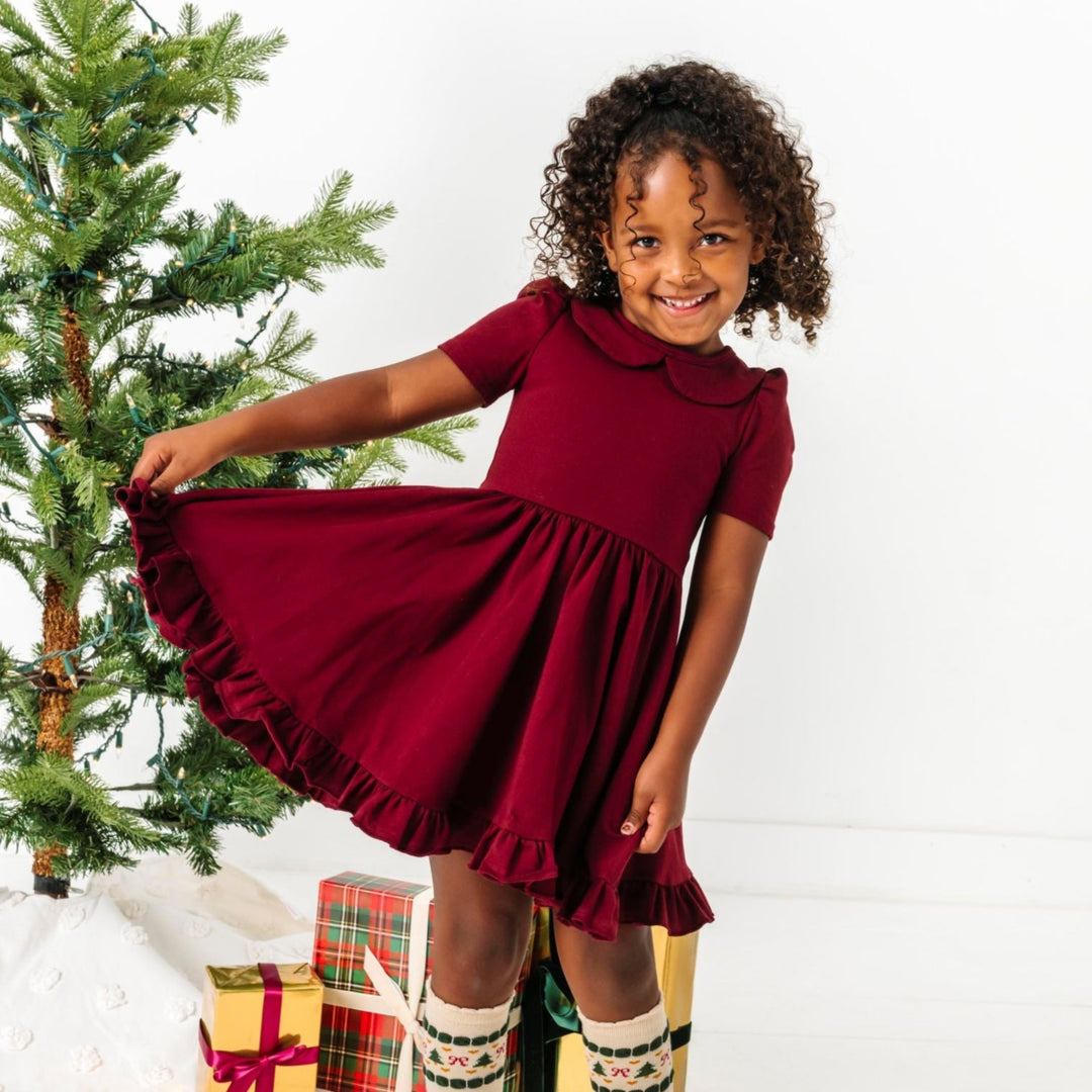 little girl posing by Christmas tree in burgundy short sleeve collared twirl dress and matching fair isle knee socks