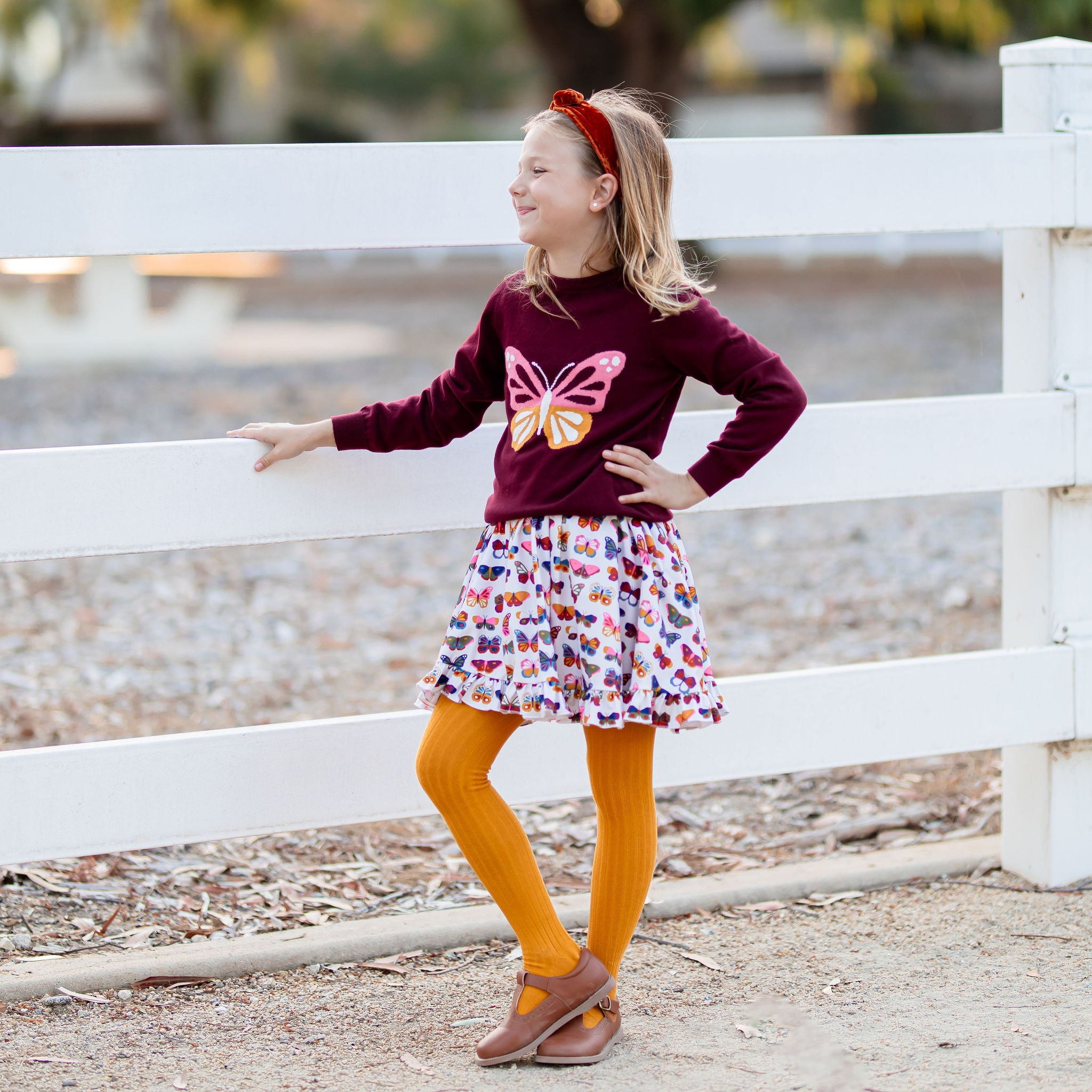 little girl wearing butterfly print dress with matching butterfly swewater and marigold yellow tights