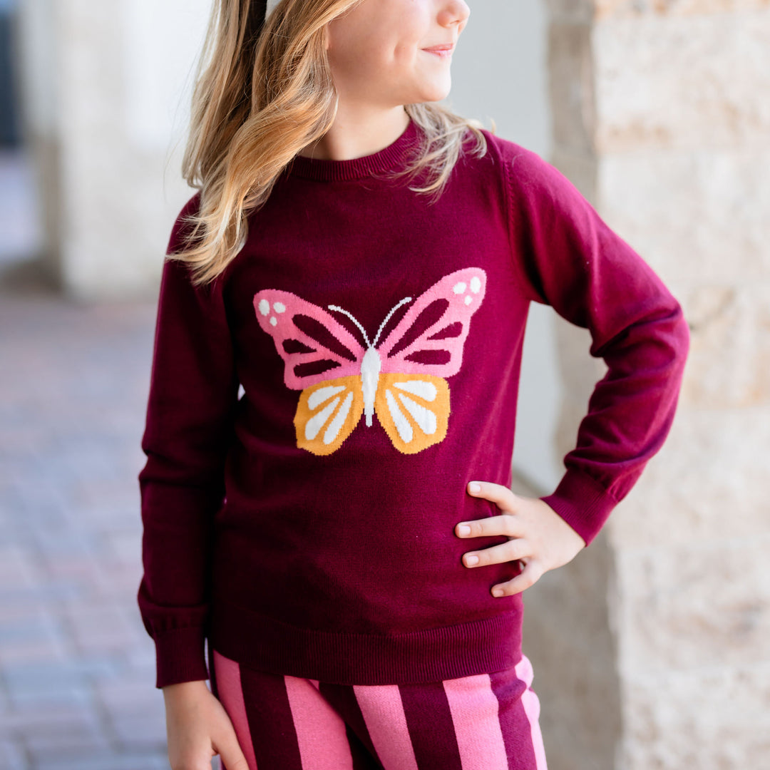 little girl with hand on hip wearing butterfly design sweater