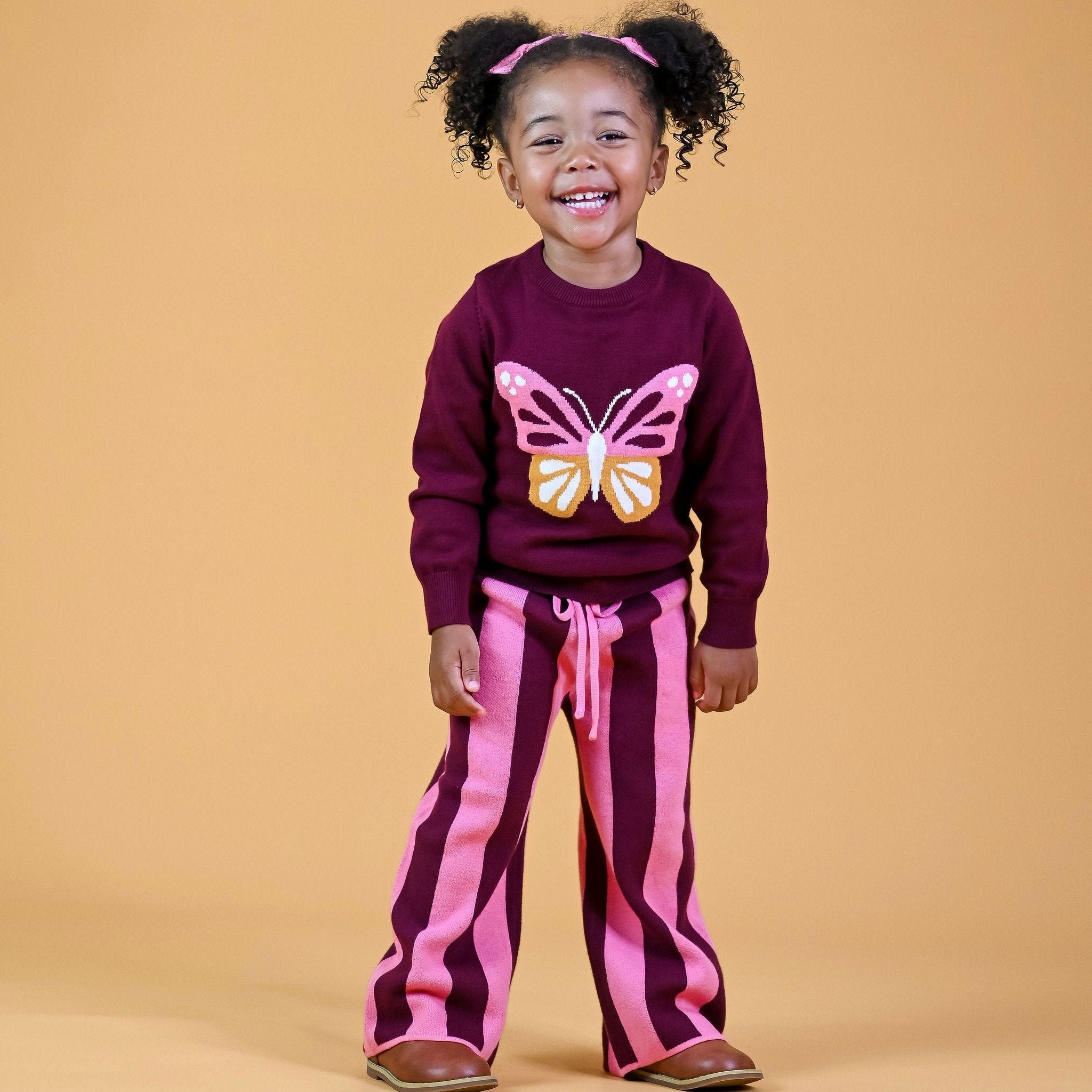 smiling little girl wearing pigtails with pink bows and butterfly sweater set