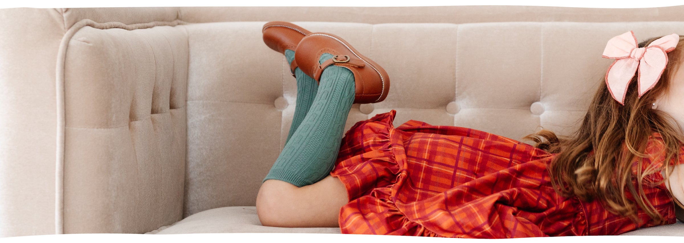 little girl on couch wearing cable knit knee high socks in teal and orange plaid twirl dress